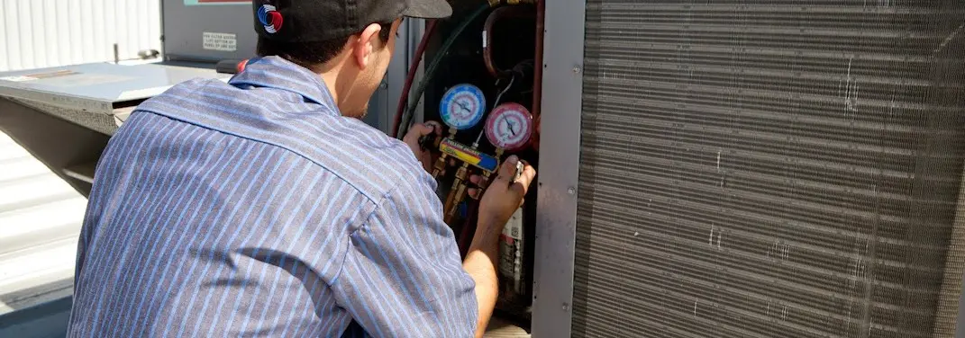 HVAC technician servicing a condenser unit in Manchester